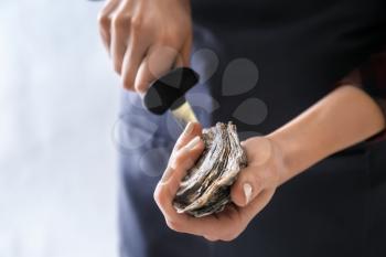 Woman opening raw oyster with knife, closeup�