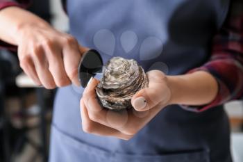 Woman opening raw oyster with knife, closeup�