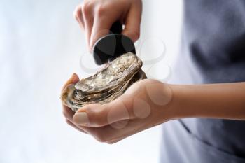 Woman opening raw oyster with knife against light background, closeup�