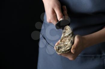 Woman opening raw oyster with knife against dark background, closeup�