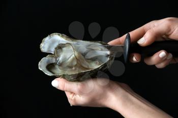 Woman opening raw oyster with knife against dark background�