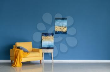 Bright armchair with pictures near color wall in room�