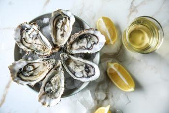 Plate with tasty cold oysters, lemon and white wine on light table�