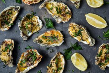 Tasty baked oysters with lemon and herbs on dark background�