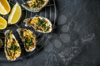 Cooling rack with tasty baked oysters and lemon on dark background�