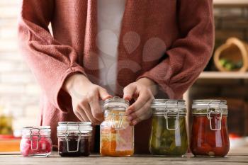 Woman with tasty fermented vegetables in jars on table�
