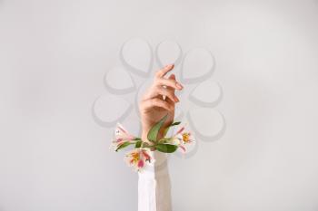 Female hand with beautiful flowers on light background�