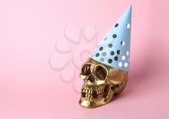 Golden human skull in party hat on color background�