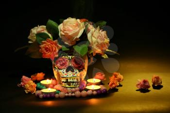 Painted human skull with burning candles and flowers for Mexico's Day of the Dead on dark background�