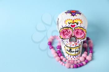 Painted human skull with beads for Mexico's Day of the Dead on color background�