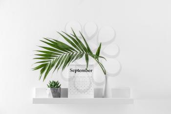 Flip calendar and vase with tropical leaf on shelf�