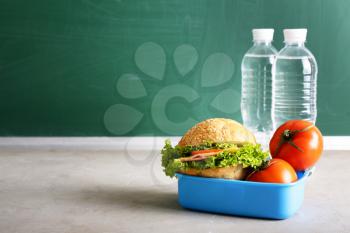 School lunch box with tasty food and bottles of water on table�