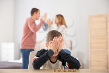 Sad little boy with coins and his quarreling parents at home. Concept of child support�