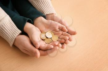 Hands of young man and his son holding coins on wooden table. Concept of child support�