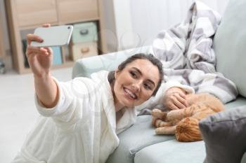 Young woman taking selfie with cute funny cat at home�