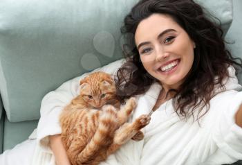 Young woman taking selfie with cute funny cat at home�