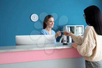 Female receptionist receiving payment for medical service from patient in clinic�