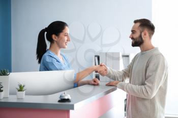 Young man and female receptionist shaking hands in clinic�