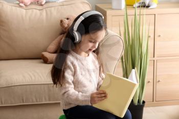 Cute girl with headphones reading book at home�