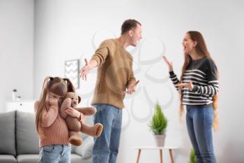 Sad little girl and her quarreling parents at home�