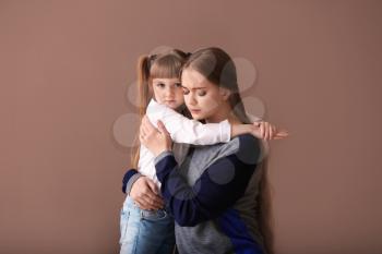 Sad woman after divorce hugging her little daughter on color background�