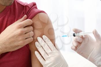 Doctor vaccinating male patient in clinic, closeup 