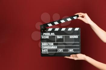 Female hands with cinema clapperboard on color background�