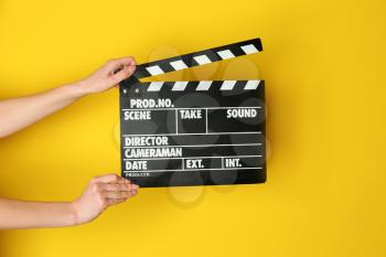 Female hands with cinema clapperboard on color background�
