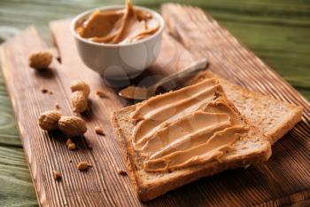Toasted bread with tasty peanut butter on wooden board�