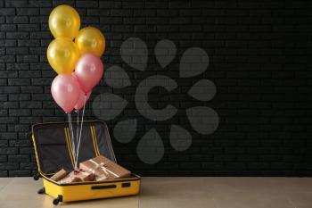 Open suitcase with gift boxes and balloons in room�