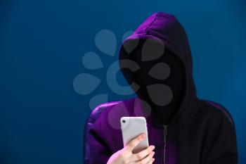Female hacker in mask and with mobile phone on color background�