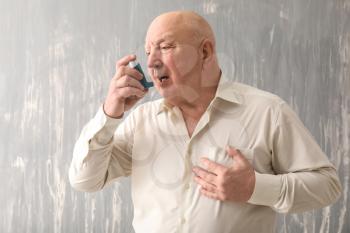 Senior man with inhaler having asthma attack on grey background�