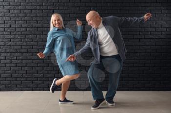 Cute elderly couple dancing against dark brick wall�