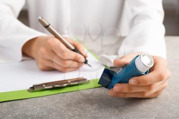 Doctor writing out prescription for using inhaler against asthma�