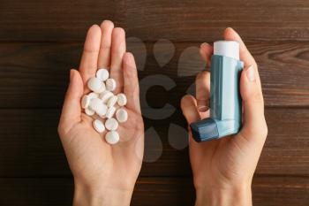 Female hands with inhaler and pills against asthma on wooden background�