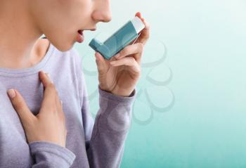 Young woman using inhaler against asthma on color background�