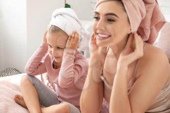 Cute little daughter with her mother after shower sitting on bed�