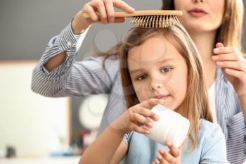 Young mother brushing hair of her cute little daughter at home�