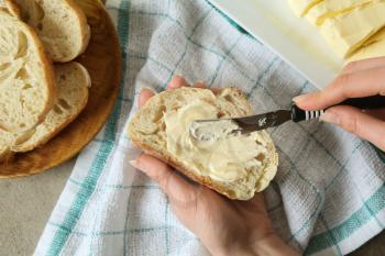 Woman spreading tasty bread with butter in kitchen�