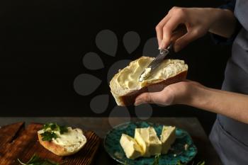 Woman spreading tasty bread with butter at table�