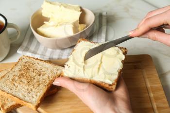 Woman spreading tasty toast with butter at table�