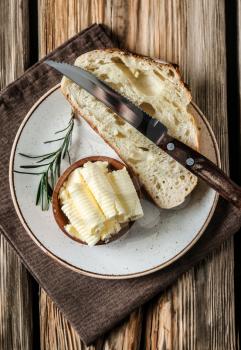 Bowl with butter curls and piece of bread on plate�