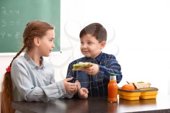 Little boy sharing his school lunch with girl in classroom�