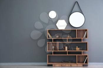 Wooden shelving unit with golden decor and mirrors on grey wall�