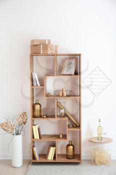 Wooden shelving unit with golden decor near white wall�