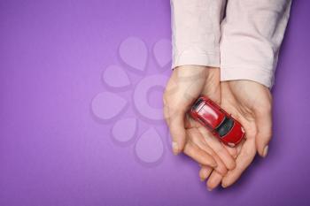Female hands with toy car on color background. Property insurance concept�