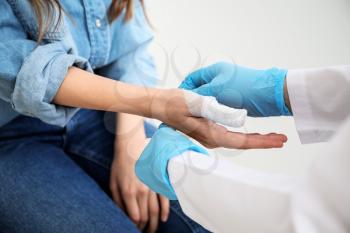 Doctor applying bandage onto finger of young woman, closeup�