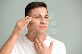 Portrait of young man with applied remedy for acne on grey background�