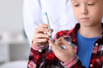 Diabetic child taking blood sample with lancet pen in clinic�