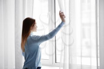 Young woman opening curtains in morning�